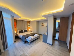 Une chambre d’hôtel moderne, dotée d’un grand lit, de tables de chevet, d’un bureau et donnant sur le couloir.