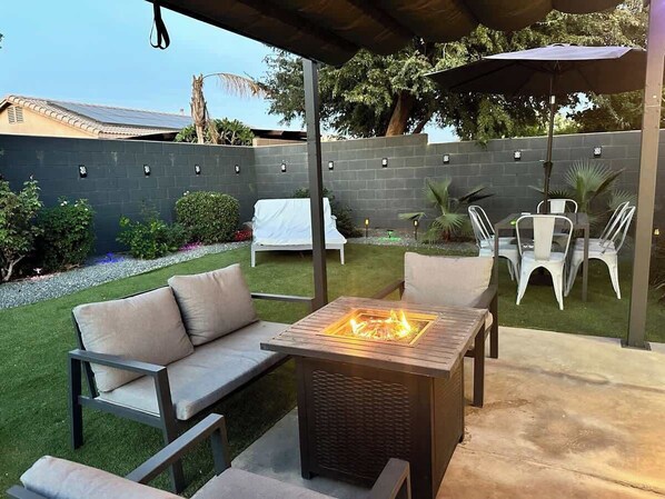 An outdoor patio with a fire pit table, seating area, and a covered section with chairs.