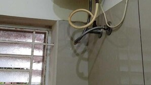 A bathroom with a water heater mounted on the wall, a window with blinds, and a shower area with a metal grab bar. - Sethu Residency (Thindukkal)