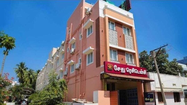 A multi-story building with a red and beige facade, a visible sign with text, and a clear blue sky. - Sethu Residency (Thindukkal)