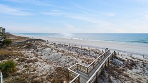 A beach with a wooden boardwalk leading to the shore, sandy dunes, and a clear blue sky.