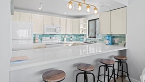 A modern kitchen with white cabinets, a large island with stools, a microwave, and a coffee maker.