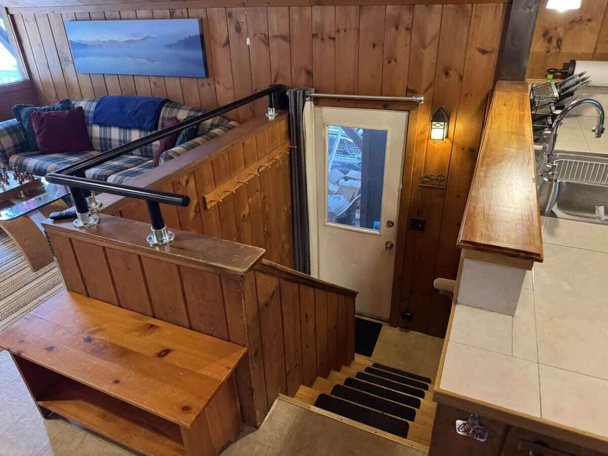 Un interior de madera con una escalera, una puerta, un banco y una zona de cocina.