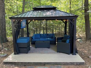 Un espace extérieur abrité avec un belvédère, des sièges rembourrés et une petite table.