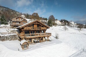 A wooden chalet with a balcony, situated on a snowy slope with a clear sky.