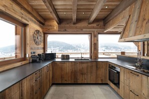 A kitchen with wooden cabinetry, a black countertop, and a large window offering a view of a snowy landscape. - LE CERF - 12 pers -Sauna-Jacuzzi (Gérardmer)