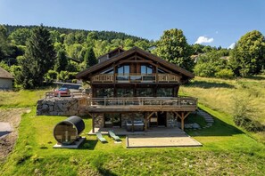 A wooden chalet with a balcony, a stone foundation, and a barrel in the foreground. - LE CERF - 12 pers -Sauna-Jacuzzi (Gérardmer)