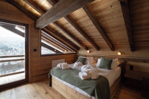 A wooden cabin bedroom with a bed, pillows, and a view of a snowy landscape through a large window. - LE CERF - 12 pers -Sauna-Jacuzzi (Gérardmer)
