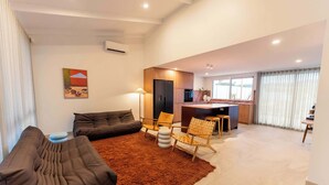 A modern living room with a sofa, chairs, and a rug. There is a kitchen area with a refrigerator and a dining table. - Hygge House - 300m to the beach (Aldinga Beach)