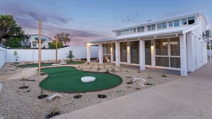 A modern building with a covered patio area, a small putting green, and a white fence in the background. - Hygge House - 300m to the beach (Aldinga Beach)