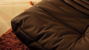 A corner of a room with a brown sofa, a patterned rug, and a tiled floor. - Hygge House - 300m to the beach (Aldinga Beach)