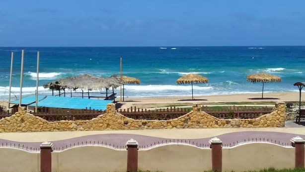 A beachside resort with a swimming pool, thatched umbrellas, and a stone wall. - Cosy homee (Alexandria Governorate)