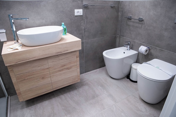 A modern bathroom with a wooden vanity, a freestanding sink, a bidet, and a toilet.