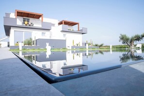 A modern two-story house with a swimming pool, reflecting the building and surrounding greenery.