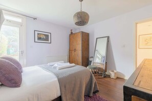 A bedroom with a bed, a wooden wardrobe, a mirror, and a window.