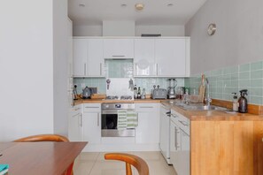 A modern kitchen with white cabinets, a wooden countertop, a stove, an oven, and a sink.