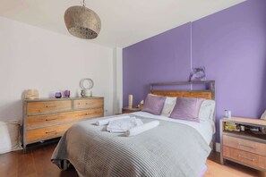 A bedroom with a bed, wooden dresser, nightstand, and a hanging light fixture. - Tranquil and Homely Flat in Stoke Newington (Greater London)