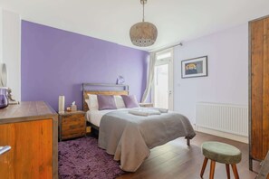 A bedroom with a bed, a wooden dresser, a purple rug, a hanging light fixture, and a framed picture on the wall. - Tranquil and Homely Flat in Stoke Newington (Greater London)