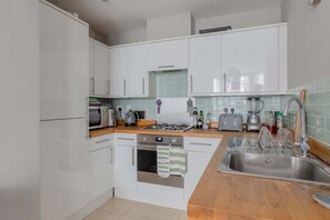 Une cuisine moderne avec des meubles blancs, un évier en acier inoxydable, un four à micro-ondes, une cuisinière et un grille-pain.