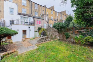 A residential area with terraced houses, a small garden with a table and chairs, and a wooden fence. - Tranquil and Homely Flat in Stoke Newington (Greater London)