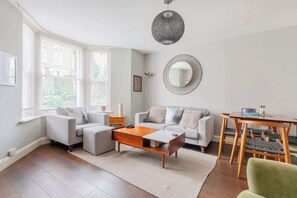 A modern living room with a sofa, a coffee table, a dining table with chairs, a round mirror, and a hanging light fixture.