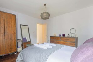 A bedroom with a bed, a wardrobe, a dresser, a mirror, and a hanging light fixture. - Tranquil and Homely Flat in Stoke Newington (Greater London)