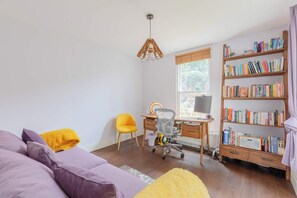 A room with a purple sofa, a yellow chair, a wooden desk with a chair, a bookshelf, and a hanging light fixture. - Tranquil and Homely Flat in Stoke Newington (Greater London)