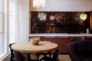 Une cuisine moderne avec un crédence en carreaux de couleur sombre, une table à manger en bois et une chaise violette.