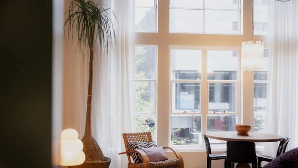 A cozy reading nook with a large window, a rocking chair, a round table, and a potted plant.