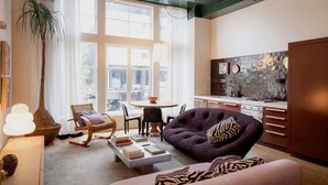 A modern living room with a large window, a dining area, and a kitchen.
