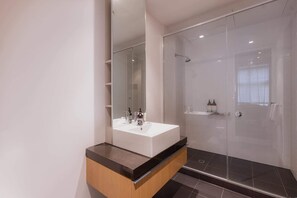 Une salle de bain moderne avec un grand miroir, un lavabo blanc et une douche à parois de verre.