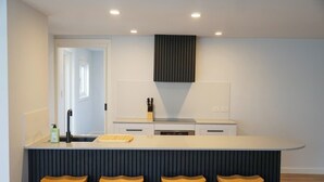 Une cuisine moderne avec un plan de travail blanc, quatre tabourets en bois et un panneau vertical foncé.