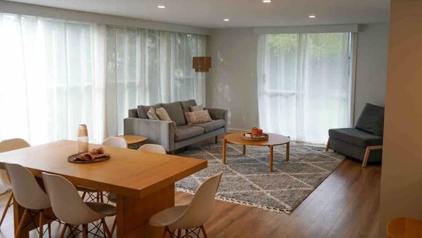 Un salon moderne avec une table à manger en bois, un canapé gris et un tapis à motifs.