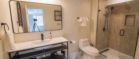 A modern bathroom with a large mirror, white sink, and a glass-enclosed shower.