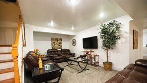 A living room with a brown leather sofa, a glass coffee table, a brown leather couch, a large potted plant, a flat-screen TV, and a painting on the wall. - Tuscan Hills Hideaway - 6 Bedrooms, 14 beds, Up to 25 people (Westminster)