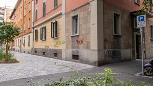 Un edificio de varios pisos con fachada roja, contraventanas verdes y un letrero de estacionamiento.