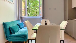 Un espacio de estar moderno con un sofá color turquesa, una mesa de comedor de cristal y sillas blancas.