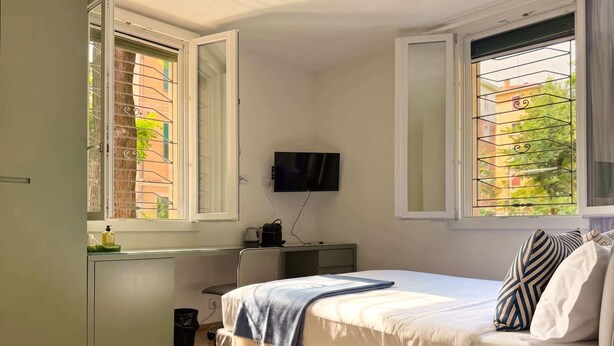 Un dormitorio con cama, mesita de noche, televisor y ventanas con rejas.