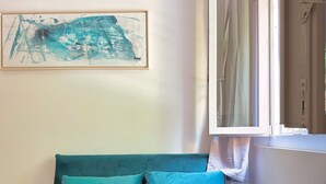 Una cama con ropa de cama color turquesa, un cuadro en la pared y una ventana con cortinas.