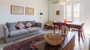 A living room with a grey sofa, a wooden coffee table with a woven basket, a red patterned rug, and a dining area with a wooden table and chairs. - Casa Melzo, with garage near Porta Venezia (Milano)