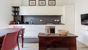 A modern kitchen with white cabinetry, a dark countertop, and a wooden dining table with chairs. There are framed pictures on the wall above the countertop. - Casa Melzo, with garage near Porta Venezia (Milano)