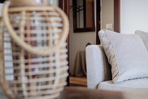 Un panier en osier avec une anse, un canapé beige avec un coussin et une table en bois dans une pièce dotée d’une fenêtre et d’un miroir au mur.