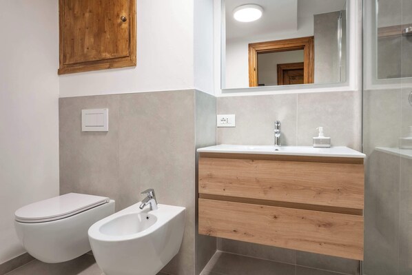 Un baño moderno con inodoro, bidé y tocador de madera con espejo.
