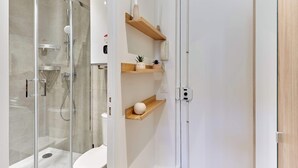 Een moderne badkamer met een douchecabine van glas, een toilet en houten planken met decoratieve objecten.