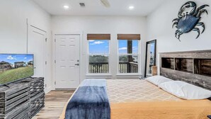 A bedroom with a bed, a television, a fireplace, and a balcony with windows. - Nautical Nest (Rockport)