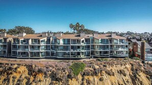 Un moderno edificio residencial de varios pisos con balcones, ubicado en un acantilado costero con vistas despejadas al océano y al paisaje circundante.