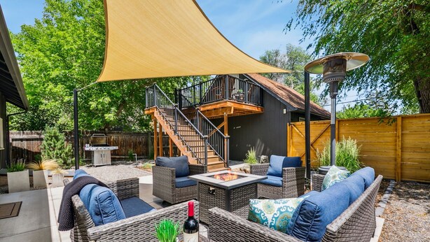 An outdoor patio with wicker furniture, a fire pit, and a staircase leading to an upper deck. - Chic Luxury Retreat in Old Town Walk Everywhere! (Fort Collins)