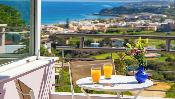 Ein Balkon mit Tisch, zwei Orangensaftgläsern und einer Blumenvase.