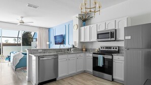 Une cuisine moderne avec des armoires blanches, des appareils en acier inoxydable, une grande fenêtre et un ventilateur de plafond.
