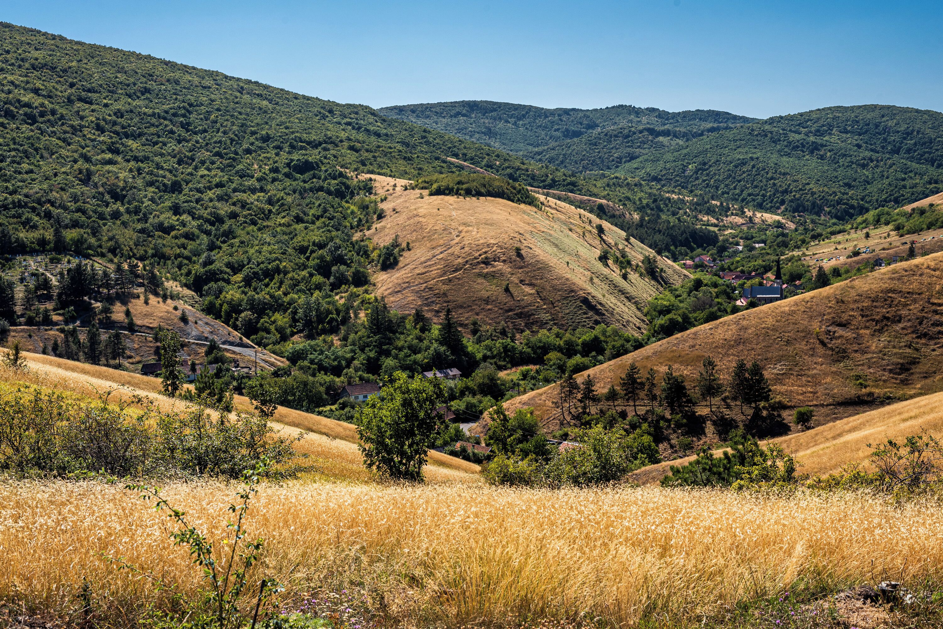 A rural landscape with rolling hills, a valley, and scattered houses.